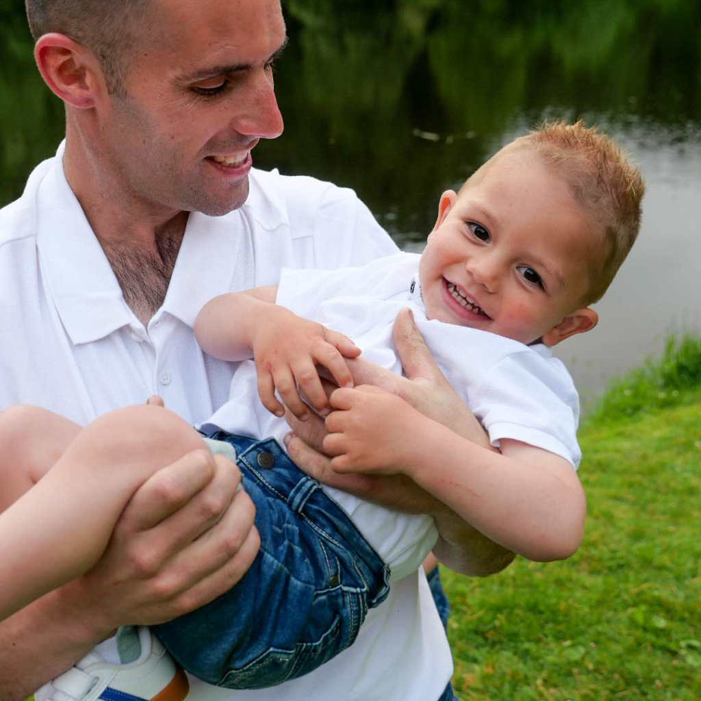 Père tenant son fils de 2 ans dans les bras lors d’un shooting photo en extérieur en lumière naturelle